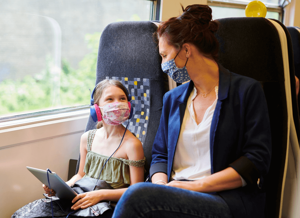A woman and a young girl sit next to each other on a train, both wearing face masks