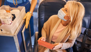 A woman with a face mask on looks up to order from a flight attendant on a plane