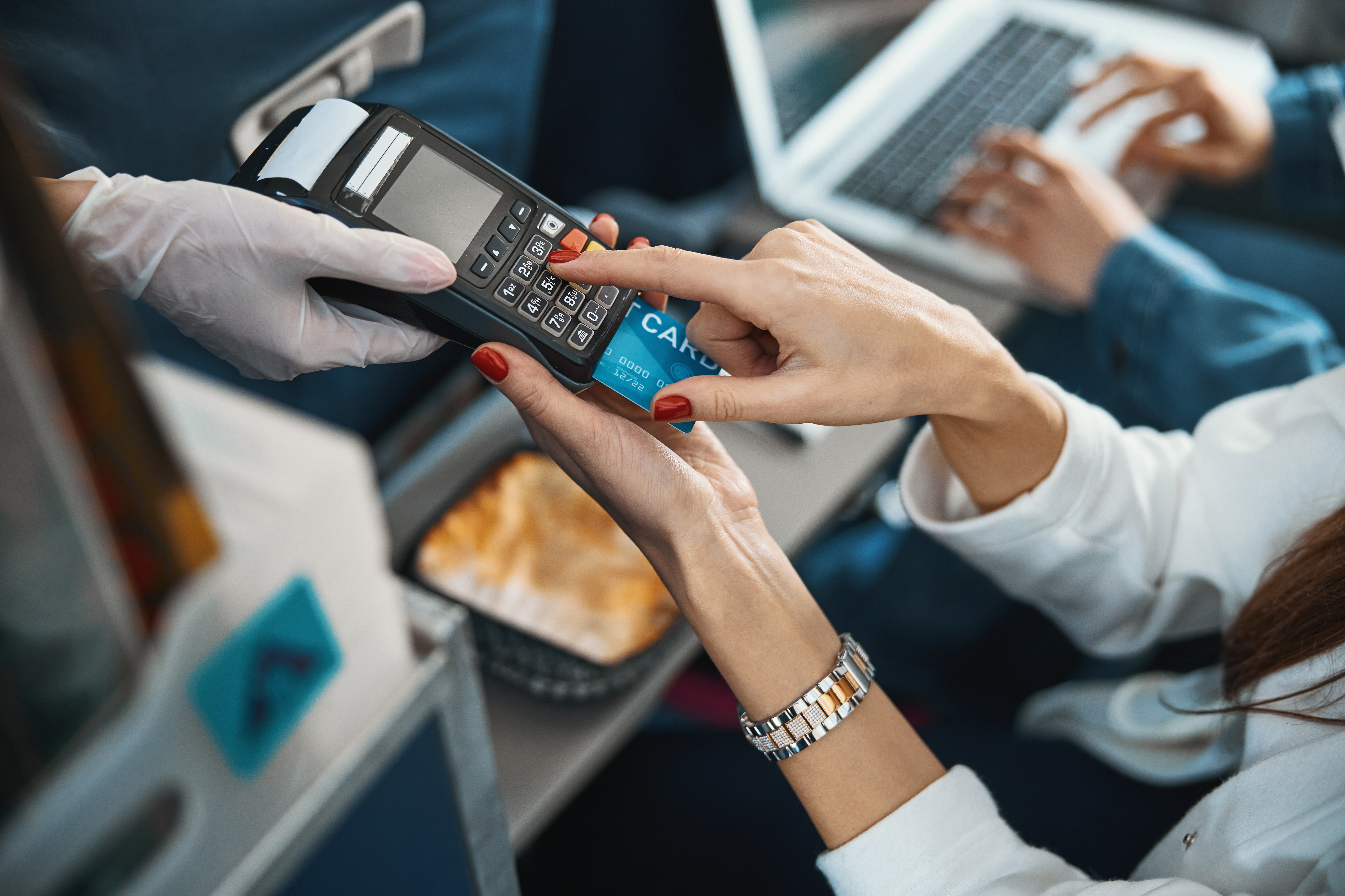 Female traveller dialing the number of her credit card, inserted into point-of-sale terminal in stewardess hand