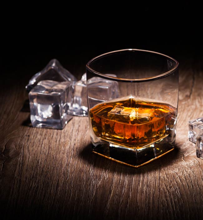 whisky glass and ice on dimly lit wood table