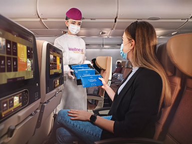 female air hostess in purple hat and PPE serving hand towels