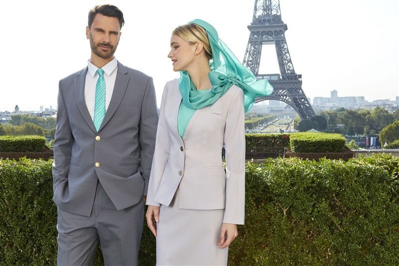 man and woman in airline cabin crew uniforms standing in front of eiffel tower