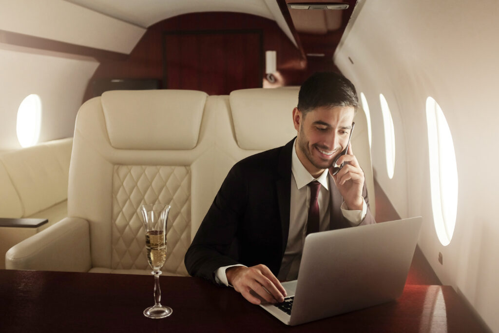 Billionaire or rich business man flying first class and working on plane with laptop and glass of champagne. Private jet concept
