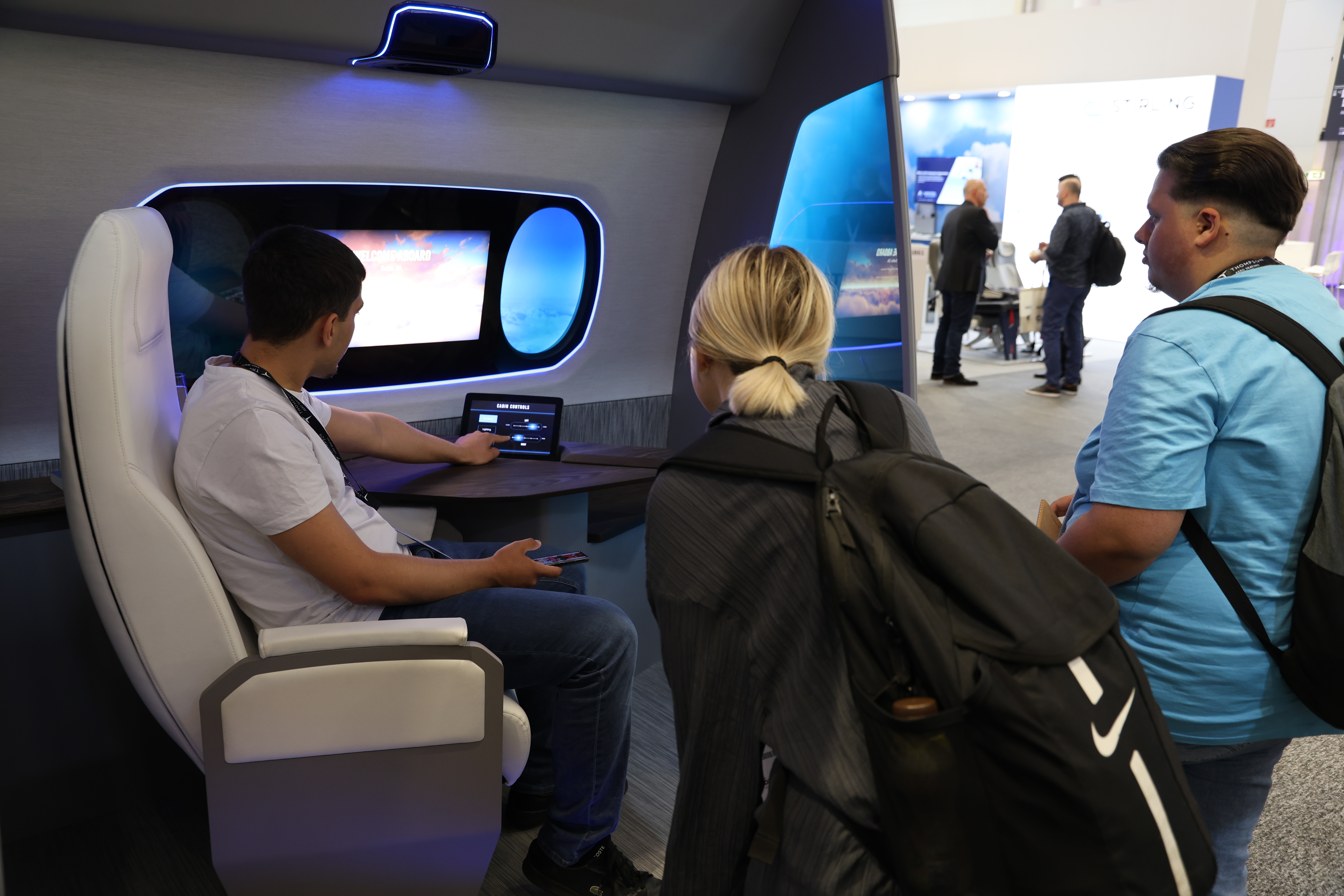 three people demonstrating inflight entertainment and connectivity hardware in a cabin mock-up